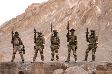 Special Forces Team Standing Together in Desert Mountain Terrain – Tactical Soldiers in Full Gear...