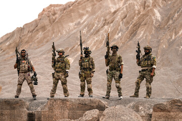 Special Forces Team Standing Together in Desert Mountain Terrain – Tactical Soldiers in Full Gear...