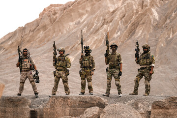 Special Forces Team Standing Together in Desert Mountain Terrain – Tactical Soldiers in Full Gear...