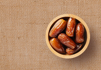 Dried date fruits in wooden bowl on brown texture background. Top view