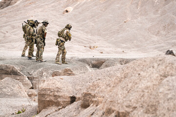 Fototapeta premium Special Forces Team Standing Together in Desert Mountain Terrain – Tactical Soldiers in Full Gear with Rifles, Communicating and Coordinating During a Military Operation or Training Mission
