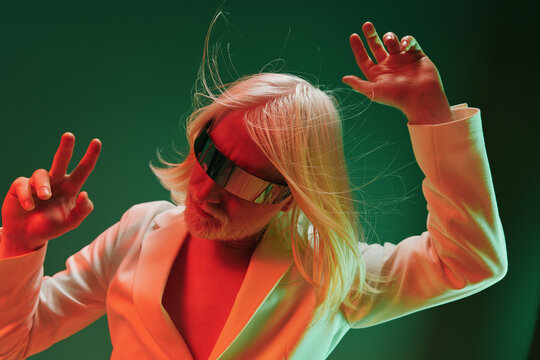 futuristic man dancing with long white hair and glasses, neon green and red background, modern vibes, expressive gestures, stylish attire, vibrant colors, energetic mood, creative atmosphere