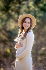 A beautiful pregnant woman is posing gracefully amidst a lush green setting, radiating immense joy and tranquility
