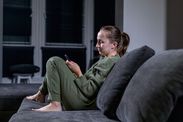 A woman is comfortably sitting on a cozy couch while looking in her phone