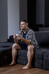 A man sits comfortably on a couch, holding a game controller
