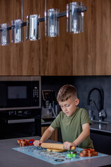Little boy rolling out gingerbread dough on the table with a rolling pin.