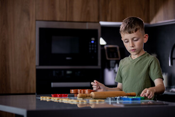 Little boy rolling out gingerbread dough on the table with a rolling pin.