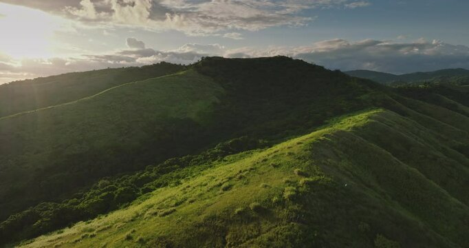 Warm sunlight bathing rolling green hills creates stunning landscape at sunset, captured aerial drone perspective, showcasing the beauty of nature and tranquility. Amazing nature travel background