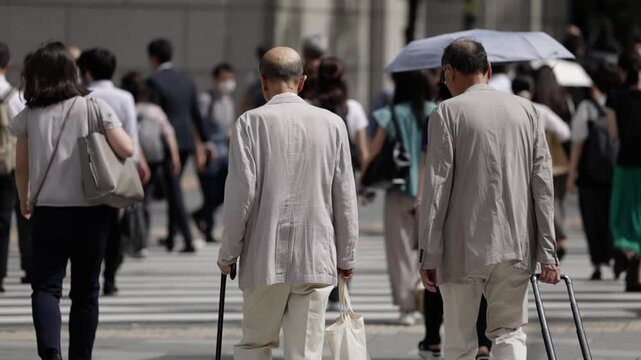 杖をついて横断歩道を渡りる高齢者男性の後ろ姿のスローモーション　東京