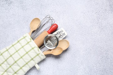 Different kitchen utensils in oven mitten on light table, top view. Space for text