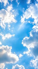 Obraz premium A vibrant sky filled with fluffy white clouds against a brilliant blue background, with sunbeams piercing through the clouds
