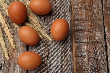 Raw eggs and spikes of wheat on wooden table, flat lay. Space for text