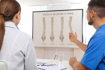 Doctors using video projector during conference about scoliosis indoors. Illustrations on...