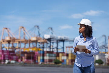 A female engineer at a shipping port shades her eyes while observing port operations. Holding a...