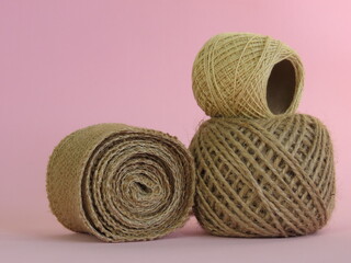 Roll of thick ecru sewing thread and roll of jute rope on light pink background. Craft threads.