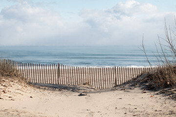 Sandy beach on blue lake in winter with snow fence and snow