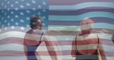 Opening with two senior women holding surfboards awaiting wave with American flag overlay - Powered by Adobe
