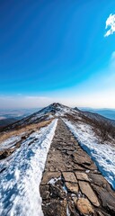 Naklejka premium Snowy mountain path leading to summit under vibrant blue sky