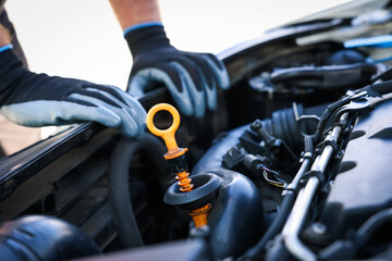 Worker checking motor oil level in car with dipstick, closeup