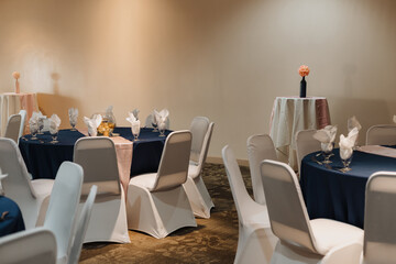 High-top cocktail table draped in half ivory and half blush linen topped with black bud vase and coral rose ball, set against navy linen dining tables with inverted glass centerpieces in reception roo