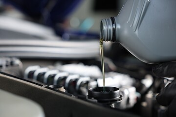 Pouring motor oil from bottle into car engine, closeup
