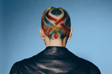 woman with colorful shaved hair design wearing black leather jacket against blue background,...