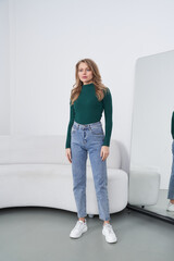 Fashion model poses in studio wearing stylish green top and blue jeans