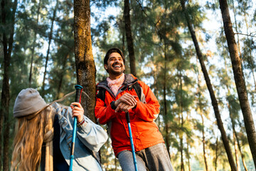 Young Couple Resting Against Tree During a Winter Hike. Enjoying the Golden Hour Light in a Peaceful Forest, Wearing Warm Clothes and Backpacks, Sharing a Quiet and Happy Moment Together