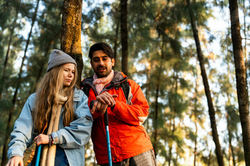 Young Couple Resting Against Tree During a Winter Hike. Enjoying the Golden Hour Light in a Peaceful Forest, Wearing Warm Clothes and Backpacks, Sharing a Quiet and Happy Moment Together