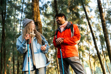Young Couple Resting Against Tree During a Winter Hike. Enjoying the Golden Hour Light in a Peaceful Forest, Wearing Warm Clothes and Backpacks, Sharing a Quiet and Happy Moment Together