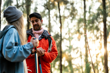 Young Couple Resting Against Tree During a Winter Hike. Enjoying the Golden Hour Light in a Peaceful Forest, Wearing Warm Clothes and Backpacks, Sharing a Quiet and Happy Moment Together
