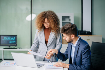 Fototapeta premium Professional man and woman collaborating on business strategy with laptops in office. Modern teamwork, corporate planning