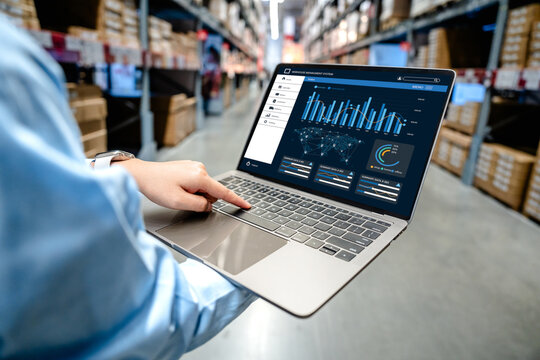 Businessman using digital warehouse inventory management dashboard system on laptop in smart warehouse, logistics technology and supply chain management concept