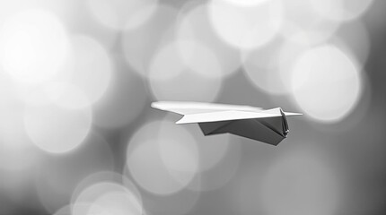 A classic black and white paper airplane sharply focused in the foreground against a soft blurred bokeh background conveying a timeless and elegant feel
