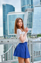 Beautiful young woman in blue skirt posing against blue sky and city buildings on sunny day. Emotions, people, beauty, travel and lifestyle concept.