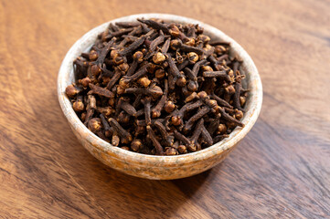 Stone bowl with dried clove buds, used for cooking and traditional medicine, close-up, spices collection