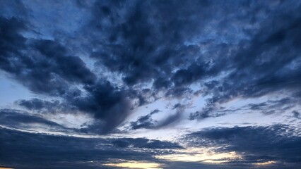 A dramatic sunrise sky filled with dark, heavy clouds in shades of blue and gray, with a band of...