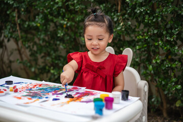 happy toddler girl painting watercolor in paper at backyard.