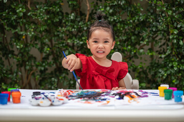 happy toddler girl painting watercolor in paper at backyard.