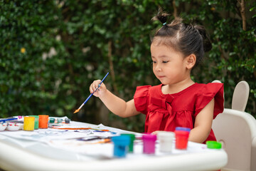 happy toddler girl painting watercolor in paper at backyard.