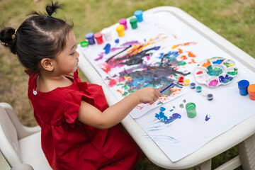 happy toddler girl painting watercolor in paper at backyard.