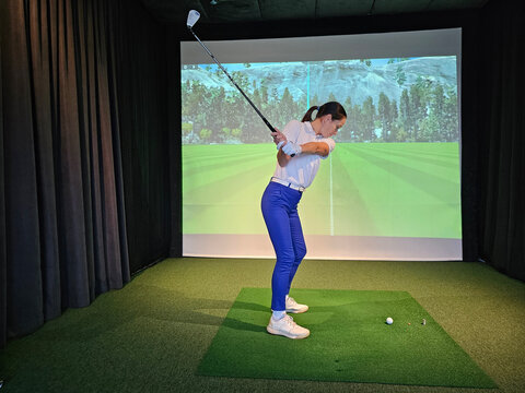 Golfer practicing swing indoors at virtual driving range with simulated landscape backdrop concept