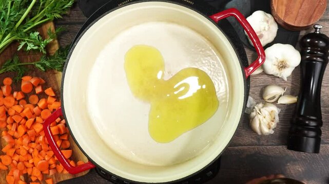 Cooking dinner and adding extra virgin olive oil to a red stock pot surrounded by fresh vegetables and herbs. Close up of pouring olive oil into a pot. Cooking a meal and starting with oil to heat up