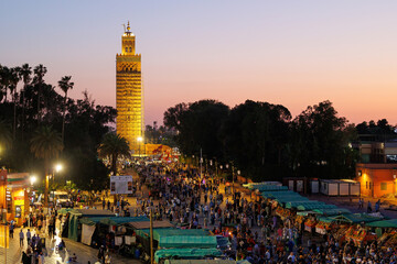 Elevated sunset street view of market stalls at Jemaa el-Fnaa in the Old Town Medina area of Marrakech with 12th century Koutoubia Mosque in the background, west Morocco 