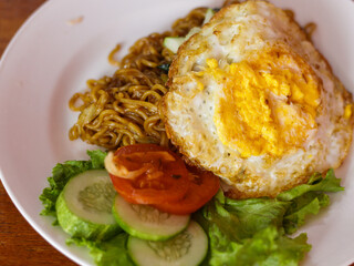 A dish of Indonesian noodles topped with a perfectly fried egg. Served on a clean white plate, this...