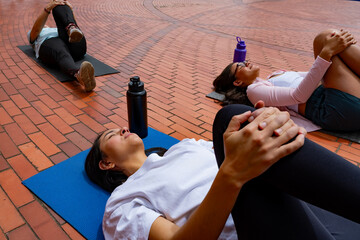 A group of Latina friends practicing yoga in a park plaza during daylight, a concept of training,...