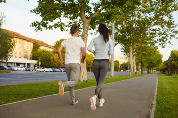 Morning run of active couple on city road, woman and man jogging together. Back view of young...