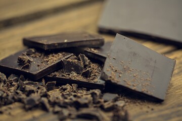 Flat design dark chocolate squares and shards are resting on rustic wooden surface, copy space