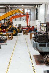 Yellow excavator loader is sitting in flat design workshop with safety tape guiding aisles