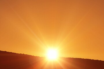 Bright sun orb shining against orange sky over hill silhouette in flat design, with starburst rays